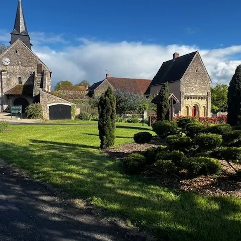 Église et prieuré de Drevant entourés d'un jardin paysager, ciel bleu.